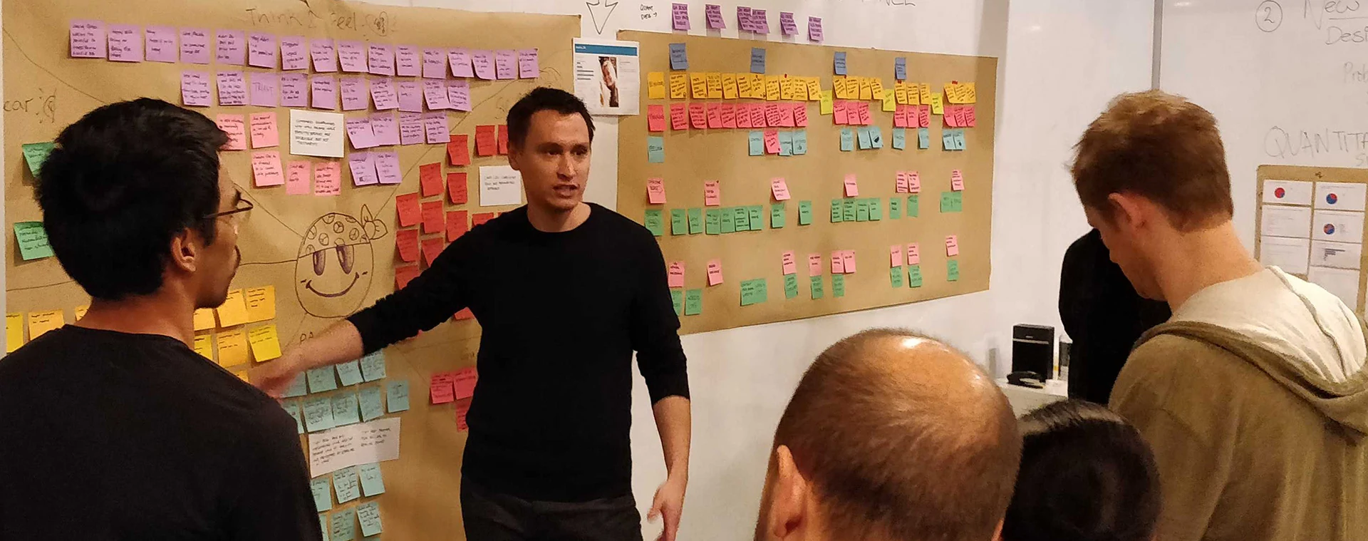 Evan presenting research findings to the team in front of walls of sticky notes