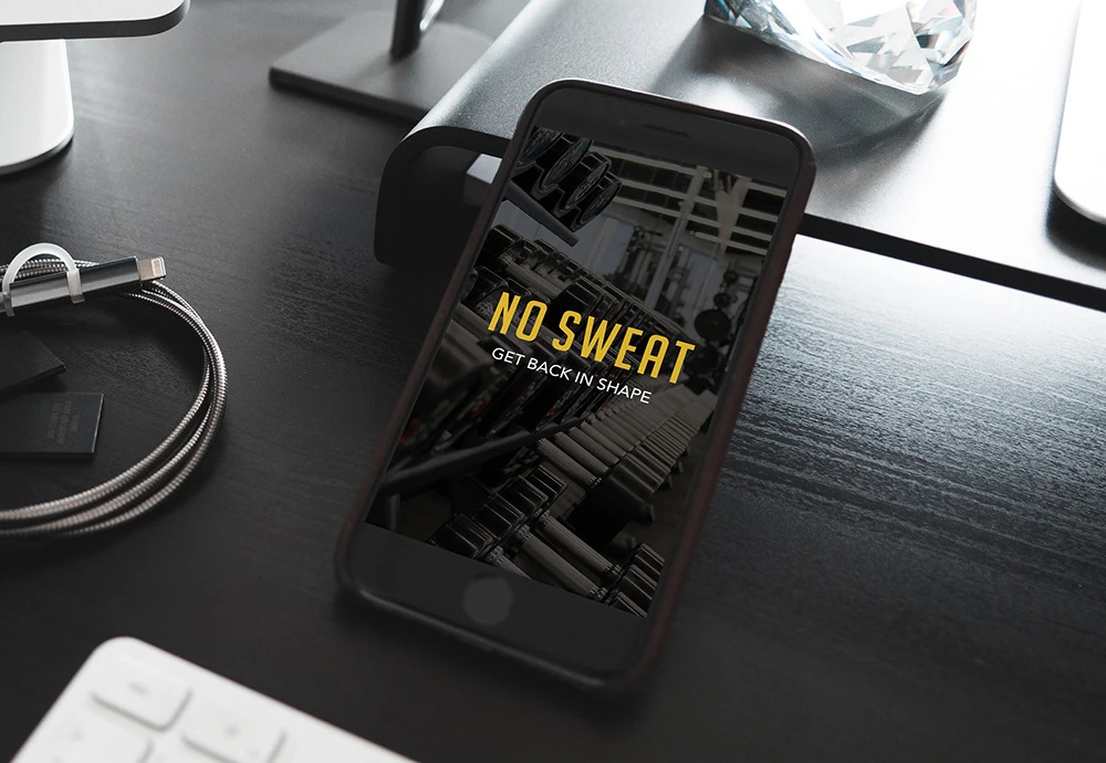 The No Sweat welcome screen on a phone resting on a dark desk