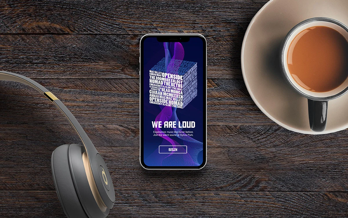 The Silent Sound welcome screen on a phone, lying on a wooden table beside headphones and a cup of coffee